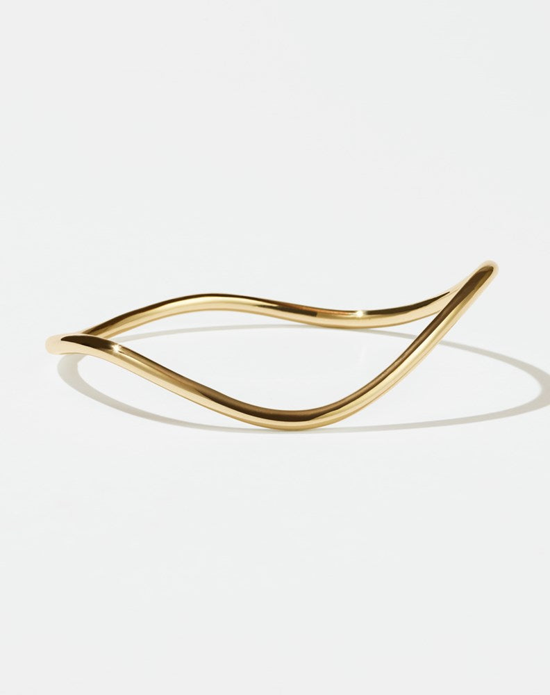 A gold-plated bracelet with a flat, minimalist design and an organic, curvy shape.