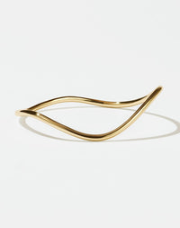 A gold-plated bracelet with a flat, minimalist design and an organic, curvy shape.