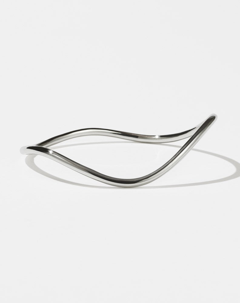 A sterling silver bracelet with a minimalist design that transitions into a curvy, rounded band.