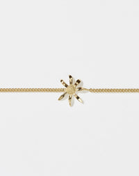 A gold bracelet featuring a daisy charm suspended between a classic curb chain.