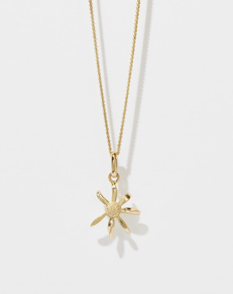 A gold daisy charm necklace on a fine chain