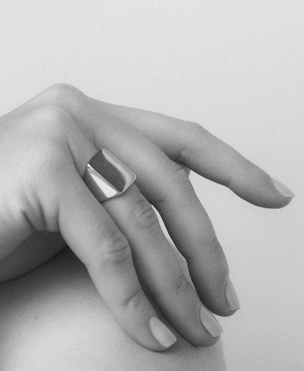 An oversized sterling silver signet ring with a flat rectangular platform for engraving, shown on a hand