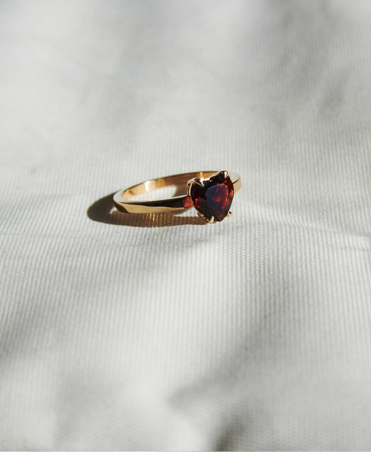 A silver ring with a heart-shaped cut garnet stone set in a simple claw setting on a delicate band. Real life