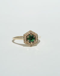 Meadowlark Jewellery’s Limited Edition Hex Engagement Ring 0.5ct in 9ct Yellow Gold, claw set with a round brilliant cut Tsavorite emerald Garnet centre stone, surrounded by a hexagon halo of pave set white diamonds. One of our most iconic and modern Ceremonial designs, made to order in New Zealand. Pair with our bestseller, the Diamond Eternity Band.