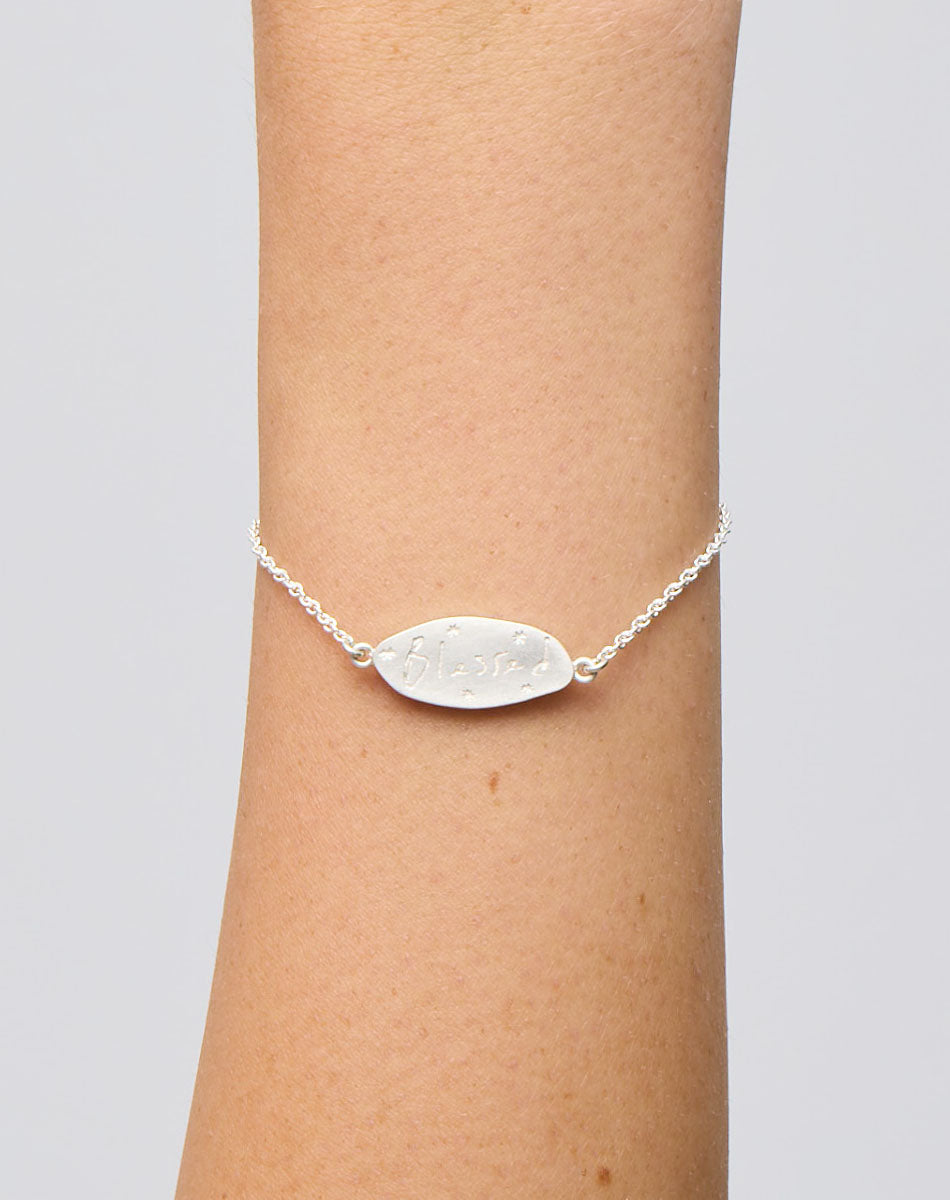 Meadowlark Jewellery’s Blessed Bracelet in Sterling Silver. A meaningful talisman for life’s journey, to serve as a daily reminder to honour the present and embrace gratitude for the quiet abundance all around us. A classic name tag in a matte, brushed texture inspired by ancient heirlooms hung from a fine diamond curb chain. From the Dreams collection. From the Dreams collection.