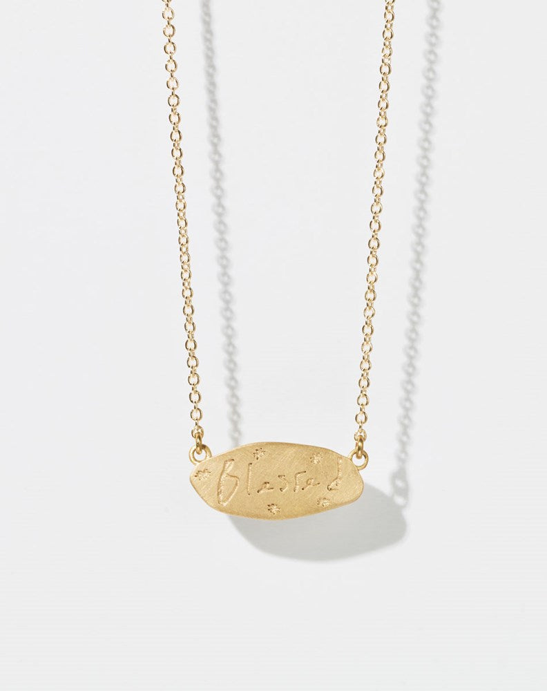 Meadowlark Jewellery’s Blessed Necklace in 9ct Yellow Gold. A meaningful talisman for life’s journey, to serve as a daily reminder to honour the present and embrace gratitude for the quiet abundance all around us. A classic name tag in a matte, brushed texture inspired by ancient heirlooms hung from a fine diamond curb chain. From the Dreams collection.