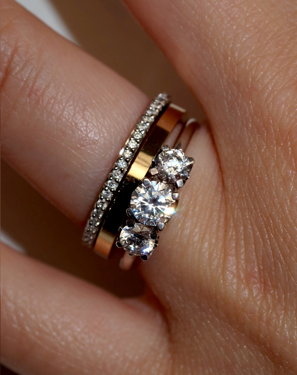 A classic three stone engagement ring in white gold with diamonds, shown on a hand with a plain band a diamond wedding band.