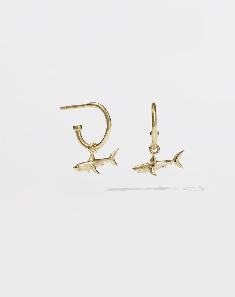 A pair of gold hoop earrings with shark charms attached