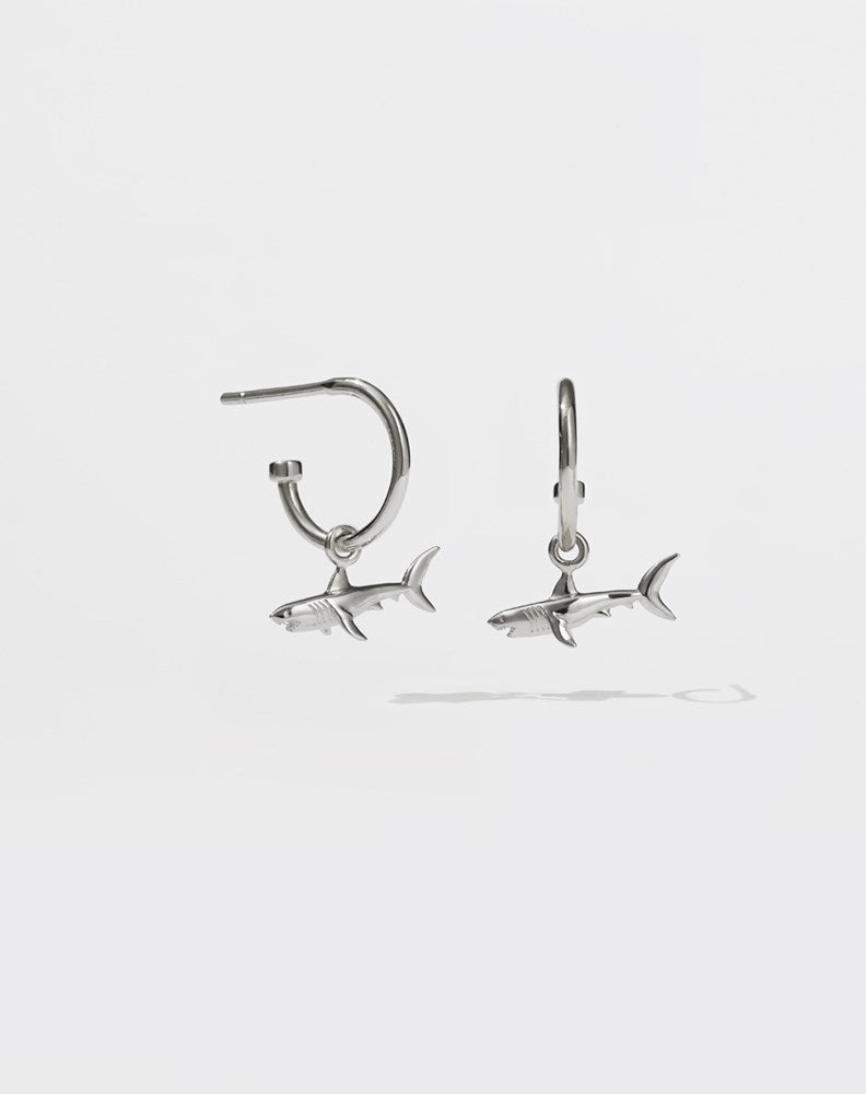 A pair of sterling silver hoop earrings with shark charms attached to them