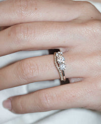 A classic three stone engagement ring in white gold with diamonds and a matching pave wedding band. On a hand.