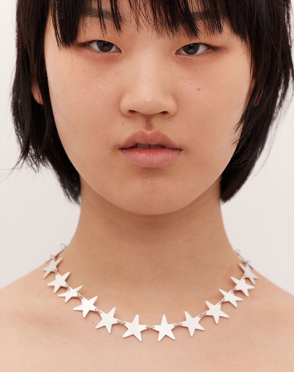 A sterling silver necklace with a series of star-shaped charms linked together. Worn on model