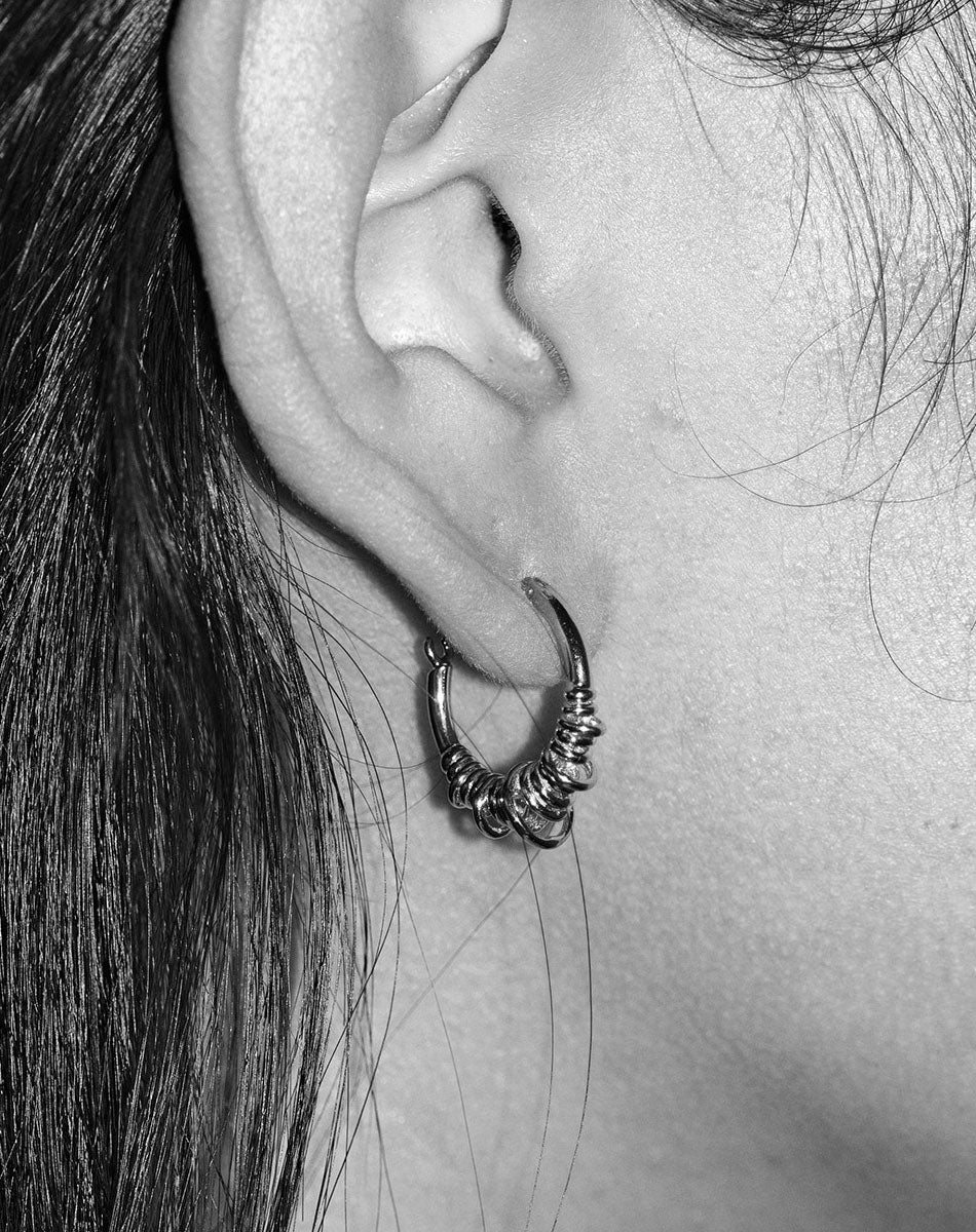 A pair of small hoop earrings made of sterling silver, with a series of rings suspended on a hoop. Worn on model
