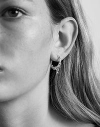 A pair of small hoop earrings made in gold, with a series of rings suspended on a hoop, with small charm. Worn on model.