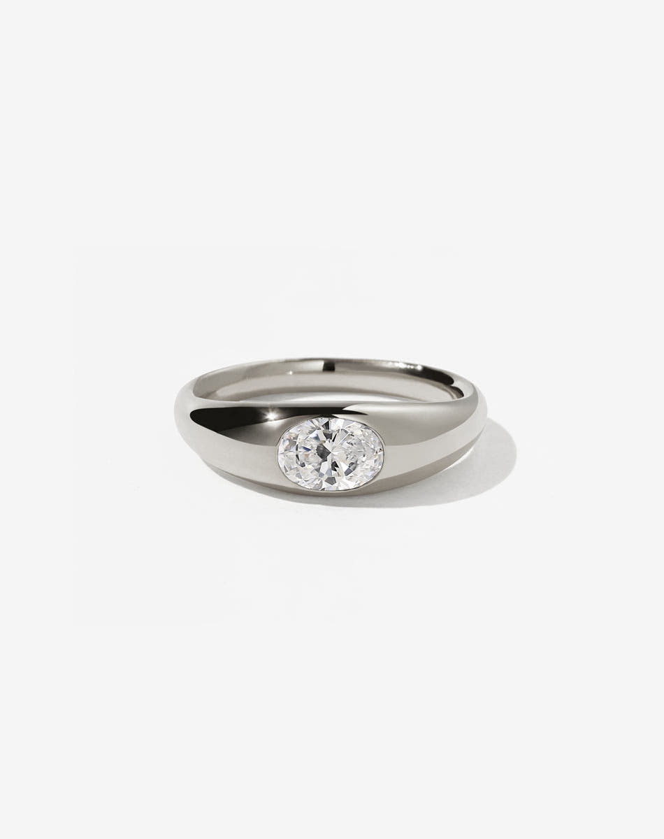An 9ct white gold ring with a central oval cut white diamond Swiss set in a smooth, rounded band.