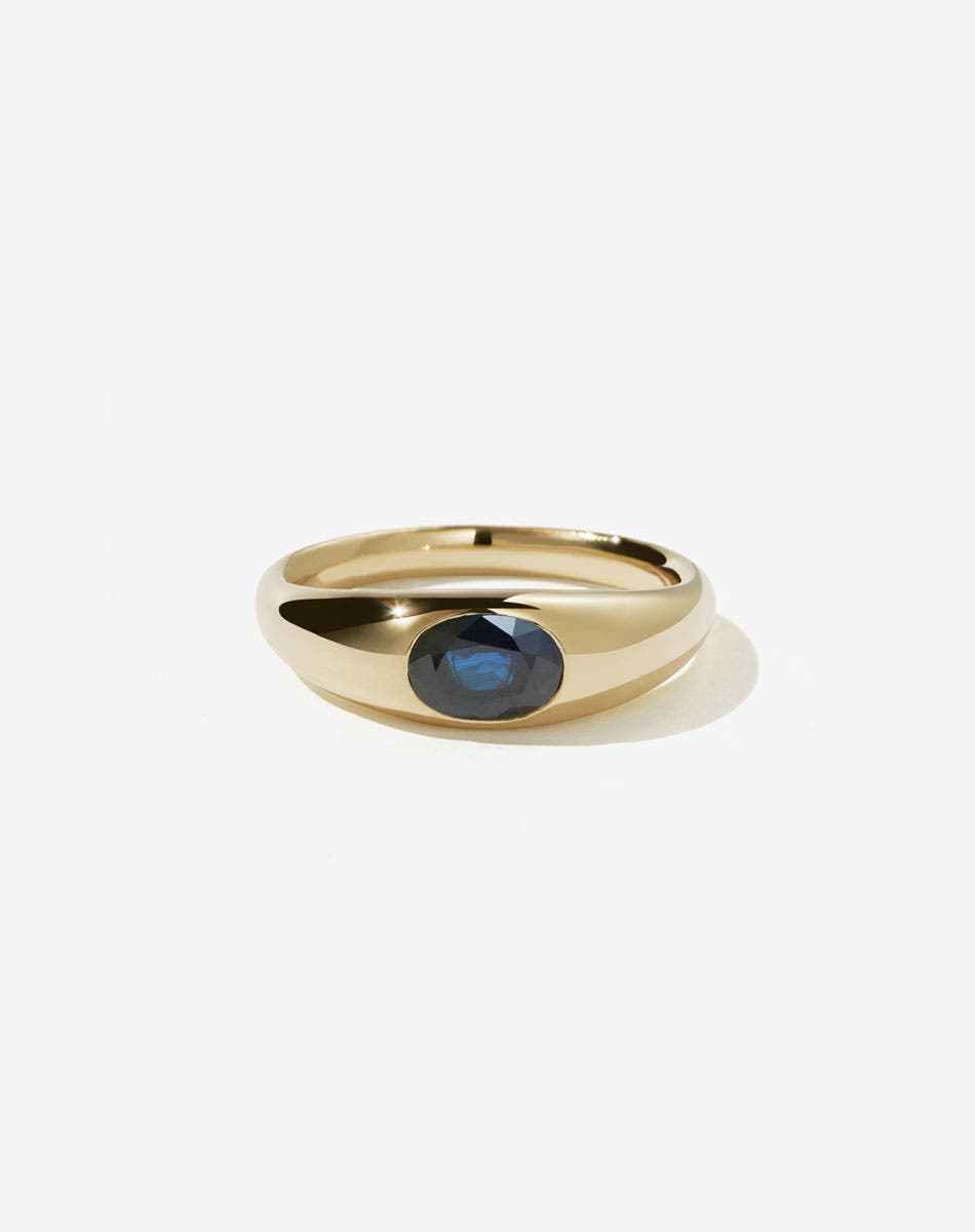 An 9ct yellow gold ring with a central oval cut blue sapphire Swiss set in a smooth, rounded band.