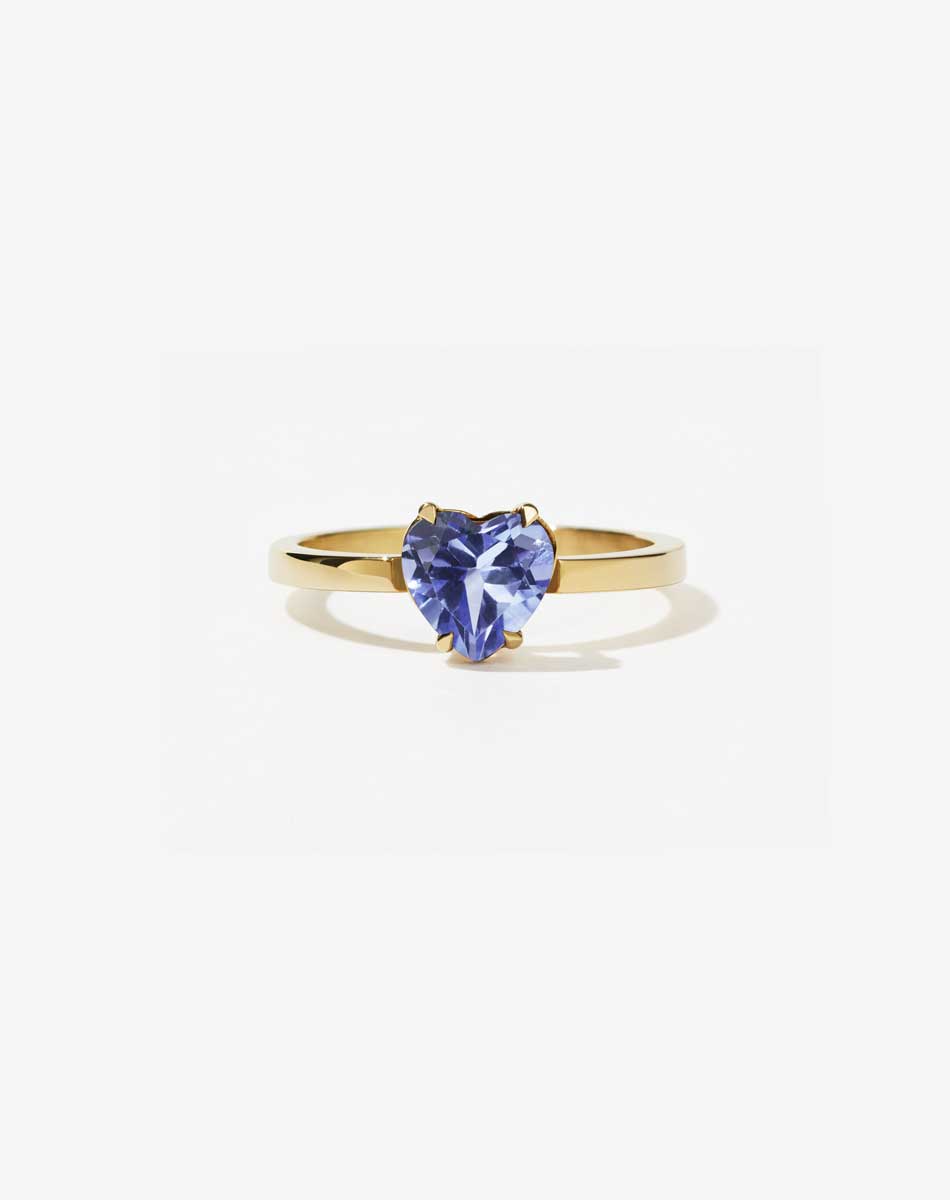 A gold ring with a heart-shaped cut tanzanite stone set in a simple claw setting on a delicate band.