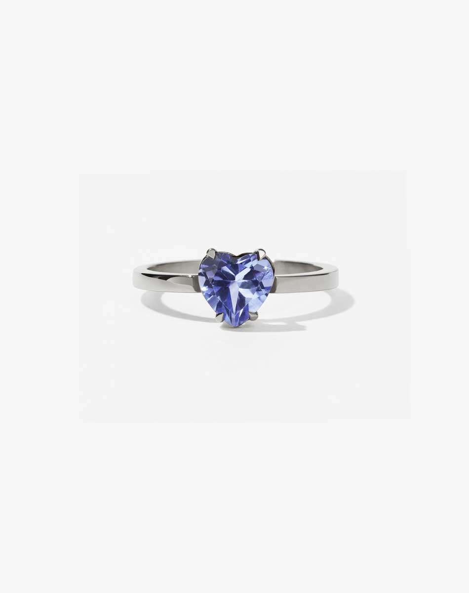 A silver ring with a heart-shaped cut tanzanite stone set in a simple claw setting on a delicate band.