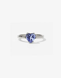 A silver ring with a heart-shaped cut tanzanite stone set in a simple claw setting on a delicate band.