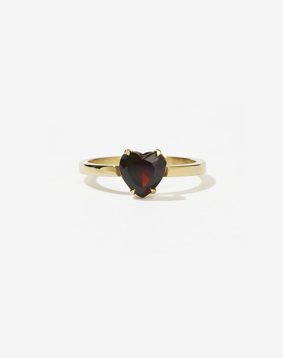 A gold ring with a heart-shaped cut garnet stone set in a simple claw setting on a delicate band.