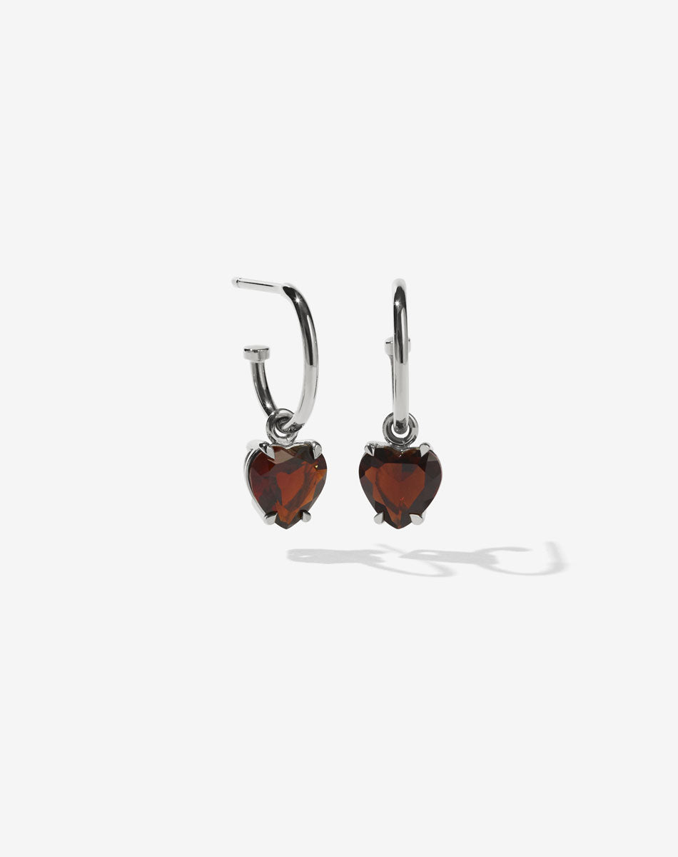A pair of sterling silver hoop earrings with heart-shaped Thai garnet stones set in a claw setting.