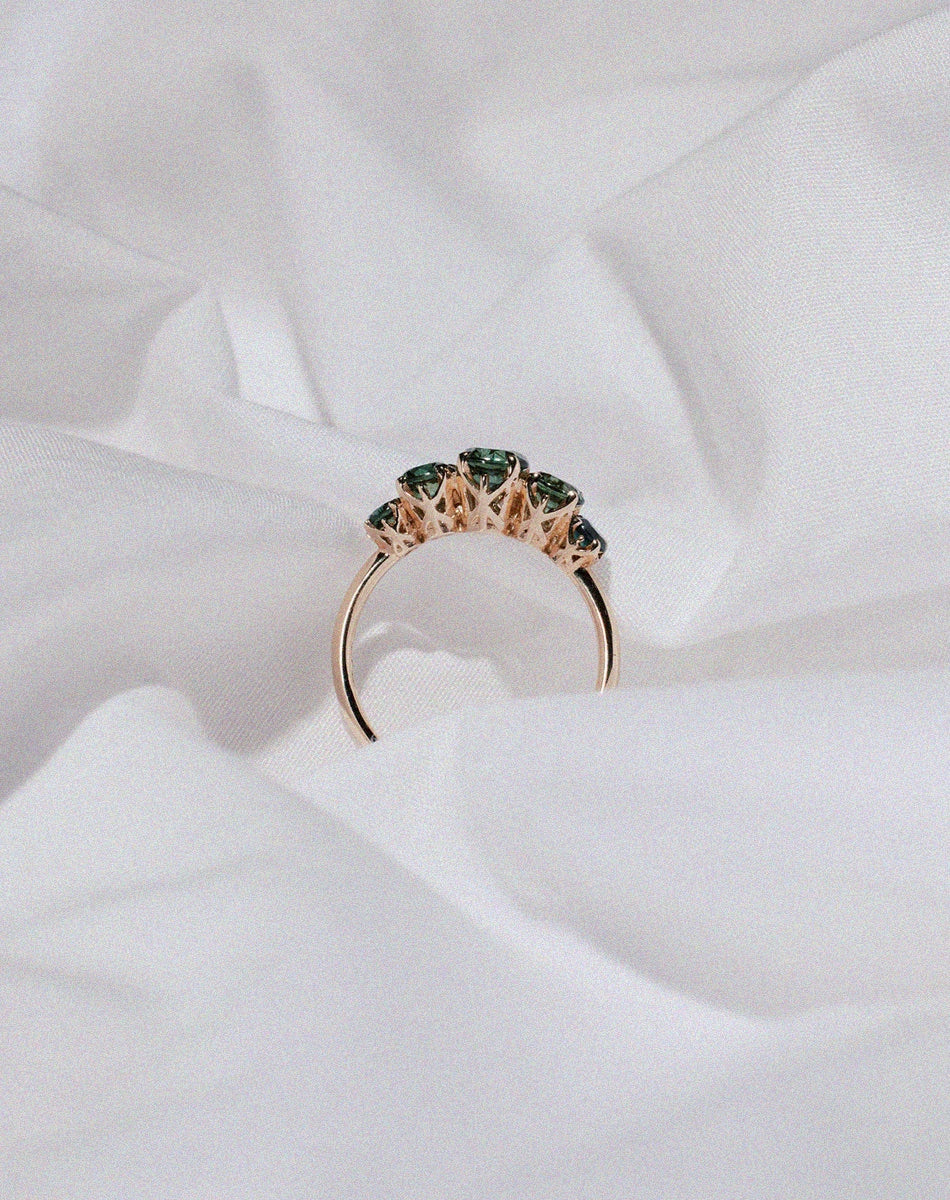 Yellow gold five stone engagement ring set with green sapphires in a decorative setting.