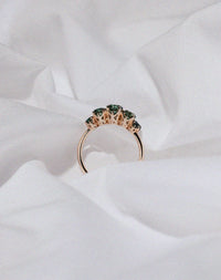 Yellow gold five stone engagement ring set with green sapphires in a decorative setting.
