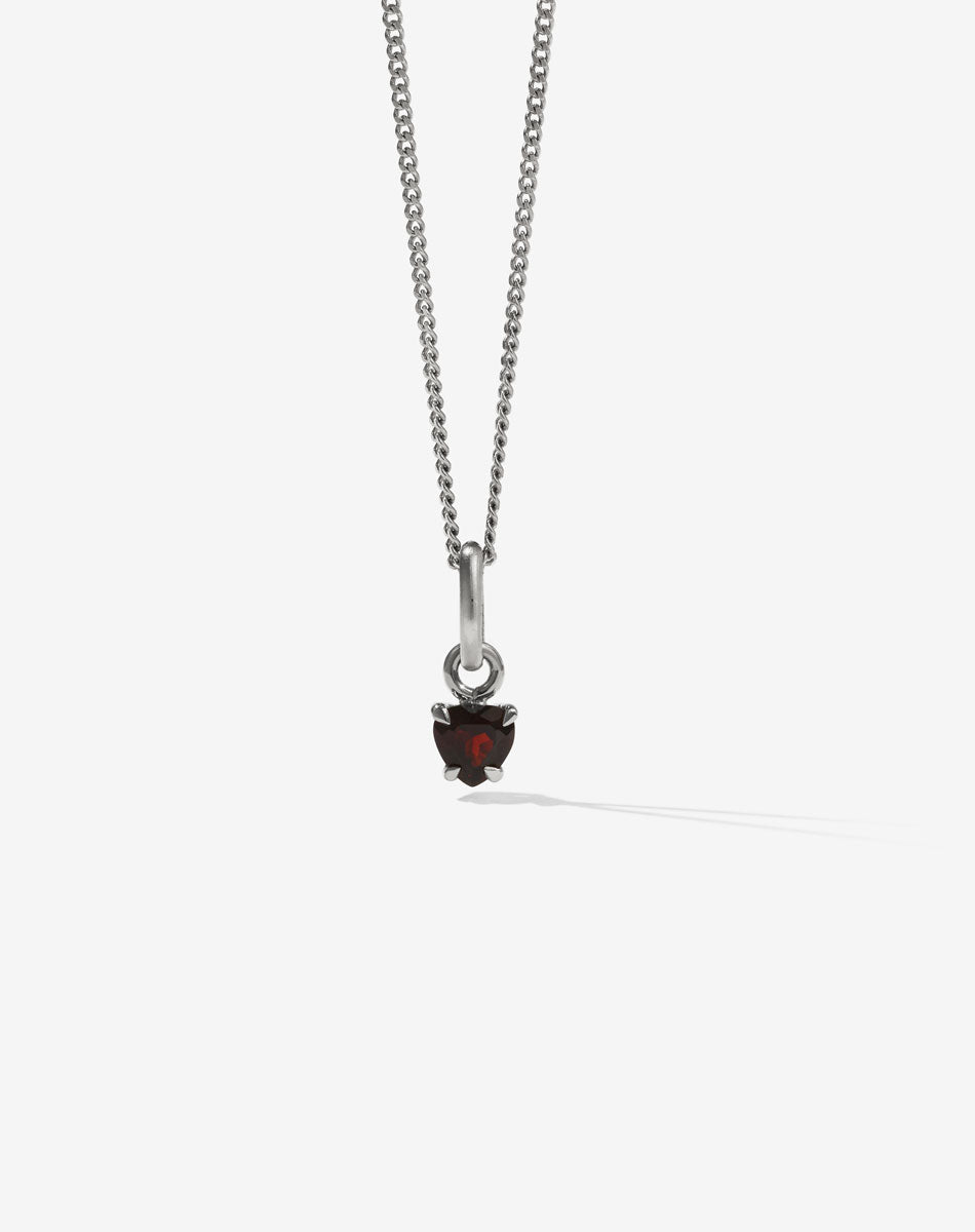 A sterling silver necklace featuring a small heart-shaped garnet stone in a claw setting, suspended from a fine chain.